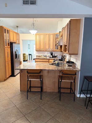 Una cocina con armarios de madera, un refrigerador de acero inoxidable, una cafetera y una isla grande con taburetes de bar.
