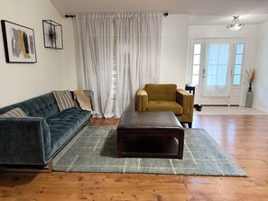 Una sala de estar con sofá, sillón, reposapiés y alfombra sobre piso de madera.