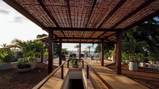 Un espacio al aire libre techado con piso de madera, plantas en macetas y vistas al paisaje.