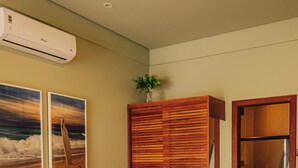 Una habitación de hotel con cama, armario de madera, ducha y dos unidades de aire acondicionado fijadas a la pared.
