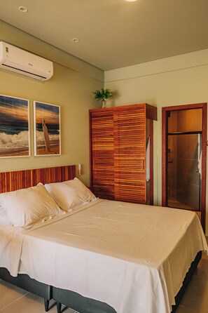 A hotel room with a bed, a wooden wardrobe, a shower, and two wall-mounted air conditioning units. - Studio Graviola with ocean view / prime location / parking / rooftop (Itacaré)