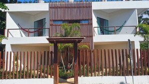 Un edificio moderno de dos pisos con fachada blanca, cerca de madera y una pequeña mesa con plantas en el frente.