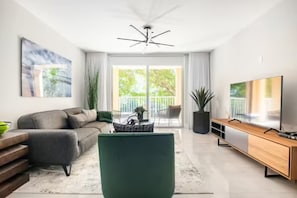 Ein modernes Wohnzimmer mit Sofa, Couchtisch, Fernseher und einem Balkon mit Pflanzen.