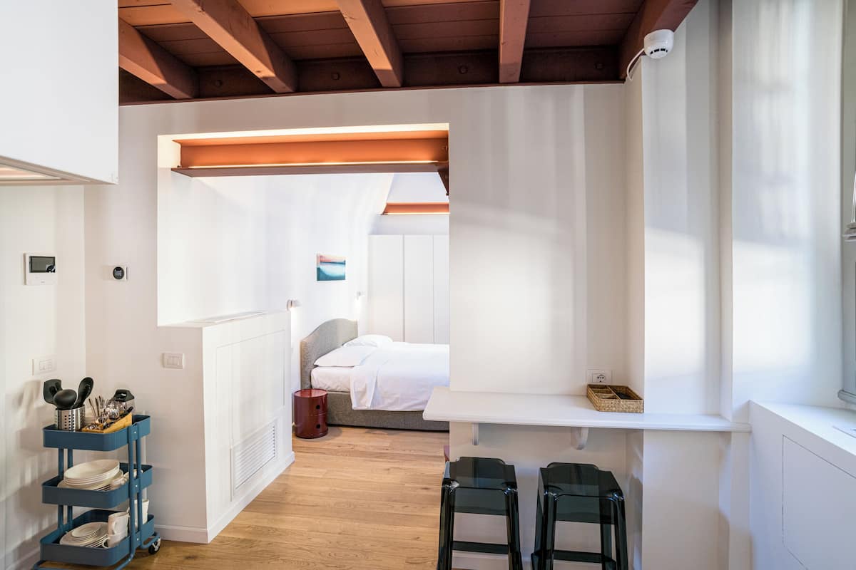 Una habitación de hotel moderna con techo de madera, cama blanca, un escritorio pequeño y una ventana.