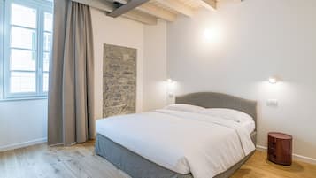 Une chambre avec un lit, un mur en pierre servant de décoration, une fenêtre avec des rideaux et un plancher en bois.