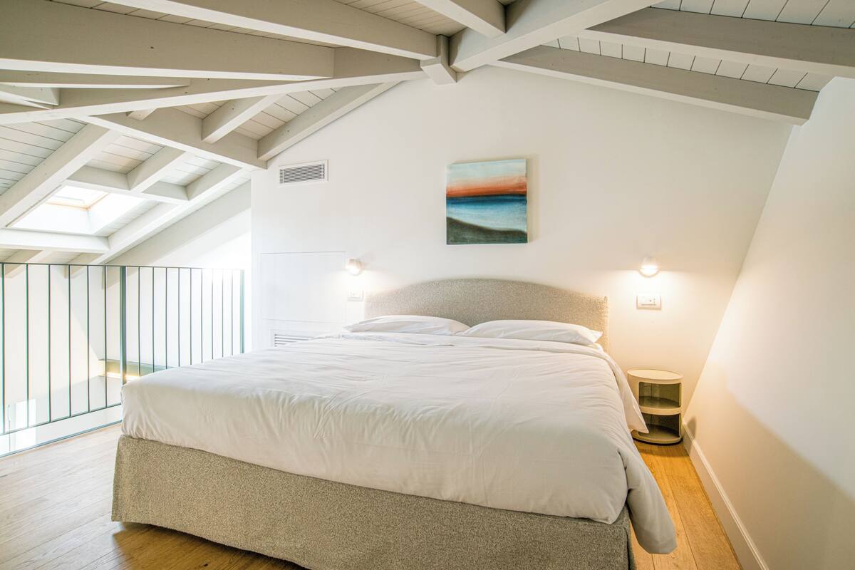 Un dormitorio con una cama grande, tragaluz y un cuadro en la pared.