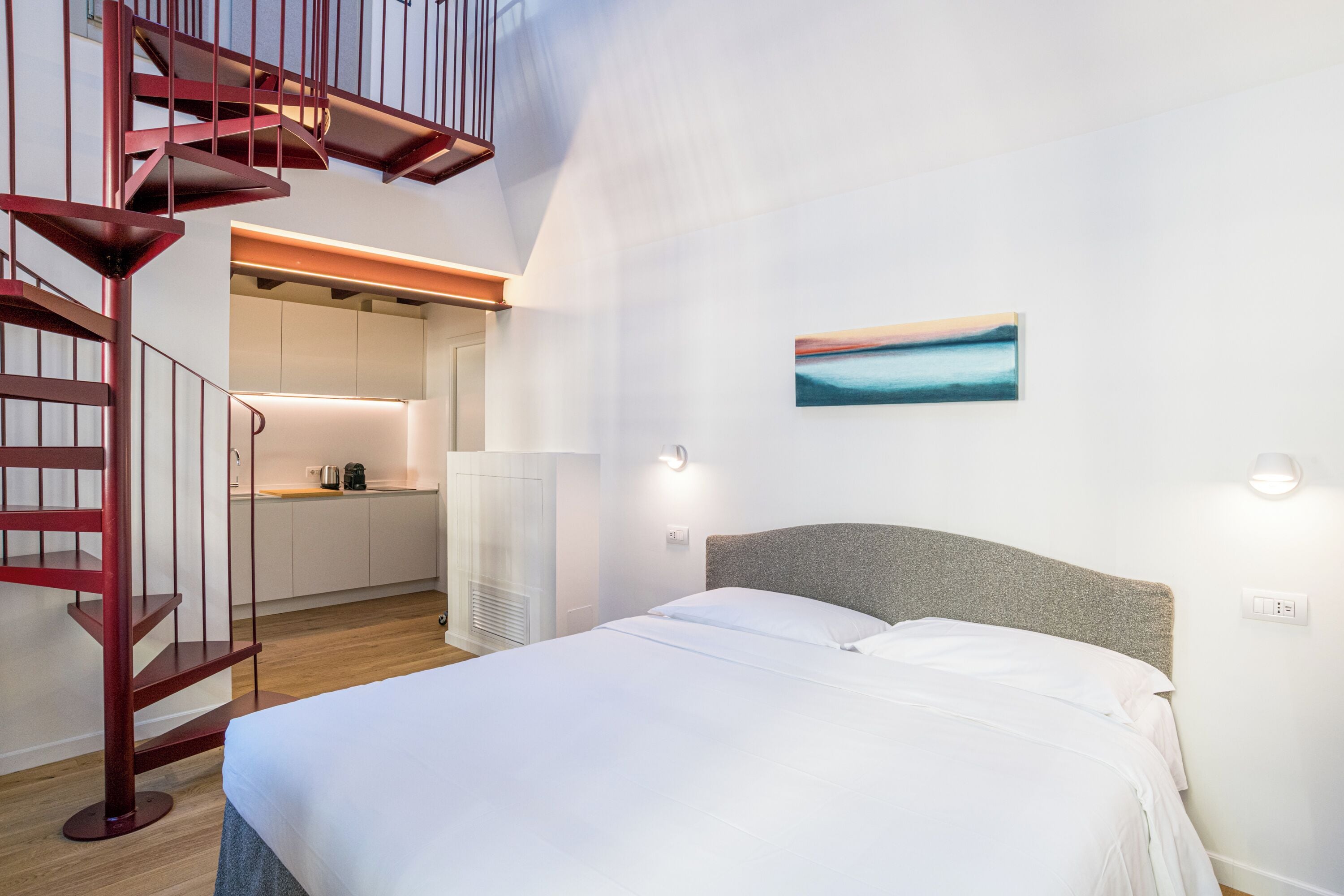 A bedroom with a bed, a staircase, and a kitchen area.