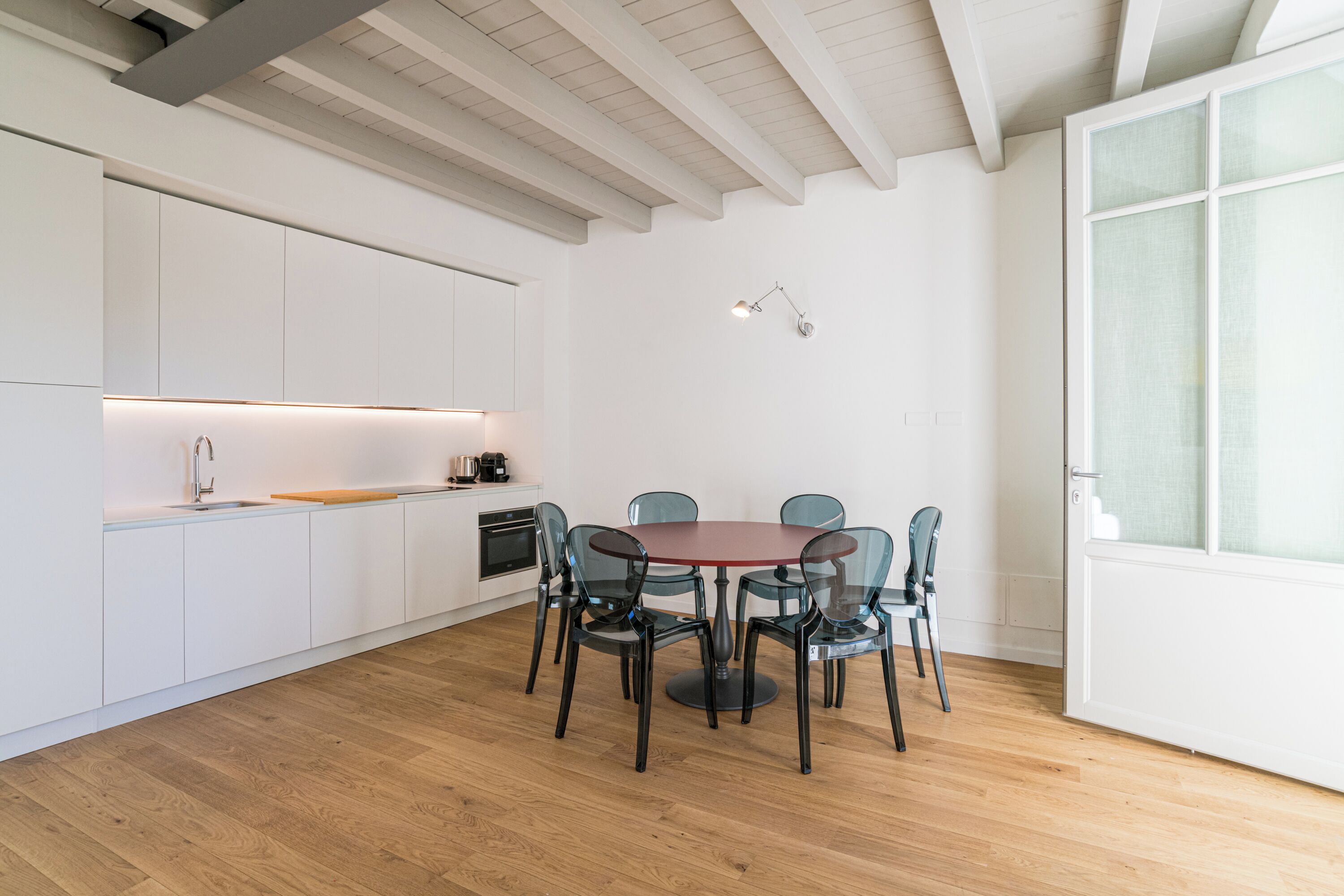 Une cuisine moderne avec des meubles blancs, un plancher en bois et une table ronde entourée de chaises.