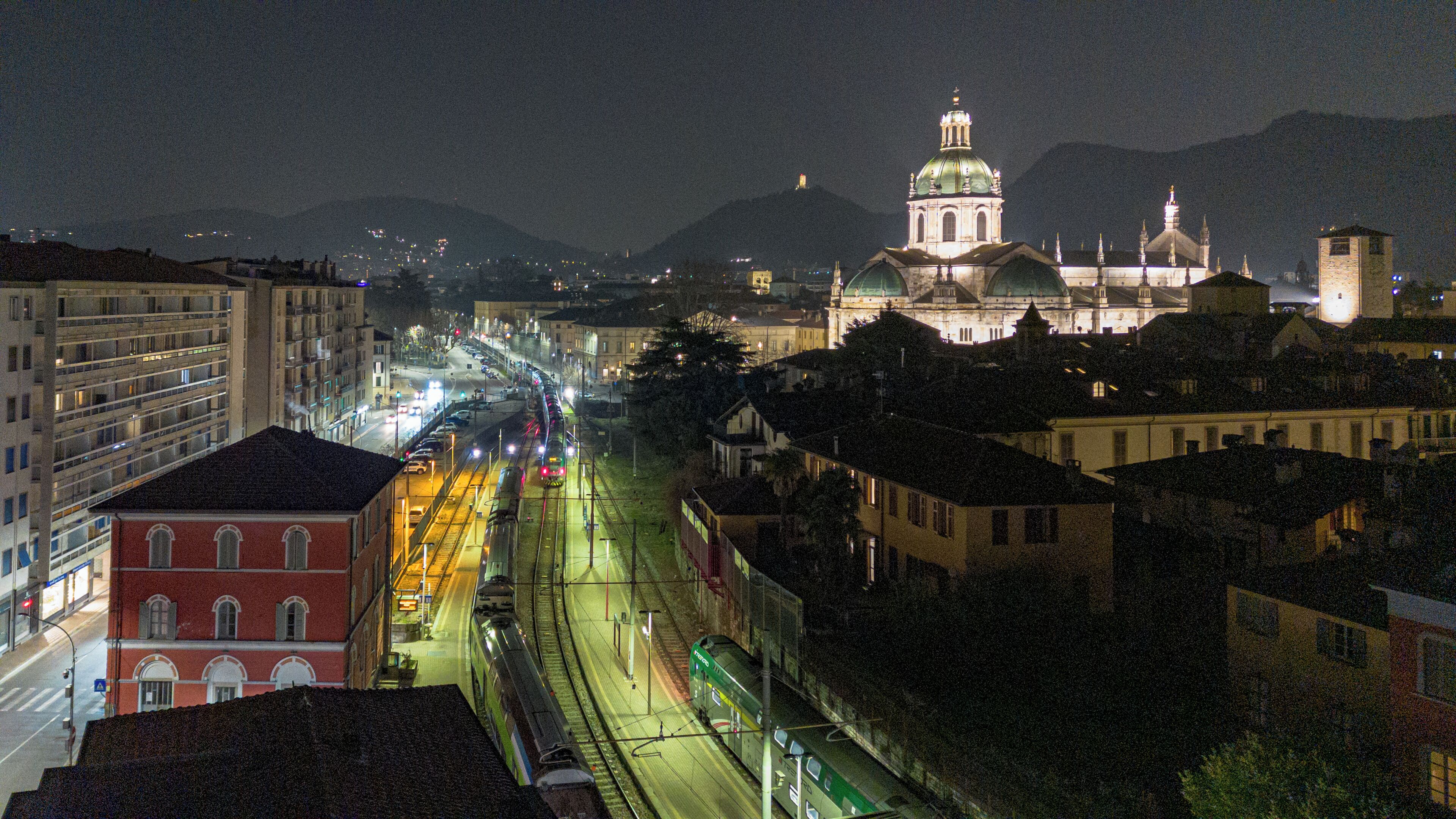 A nighttime cityscape with a train on tracks, buildings, and a prominent church with a dome.