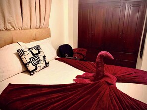 Ein Bett mit einer roten Decke, einem gemusterten Kopfkissen und einer Holztür im Hintergrund.