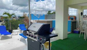 Eine Dachterrasse mit Grill, blauen Lounge-Sesseln und Blick auf das Stadtzentrum.