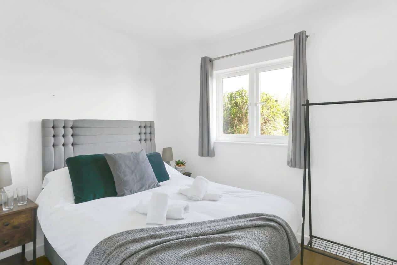A hotel room with a bed, a bedside table, a window with curtains, and a view of greenery outside.