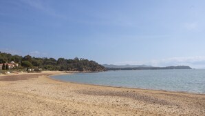 Ein Strand mit sandigem Ufer, einem ruhigen Meer und einer bewaldeten Hügelkette im Hintergrund.
