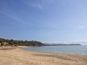 A beach with a sandy shore, a calm sea, and a forested hill in the background. - Apartment Haïti by Interhome (La Londe Les Maures)