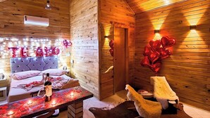 Un acogedor interior de cabaña con techo de madera, una zona de comedor con una mesa preparada para dos personas, un sofá y una alfombra grande.