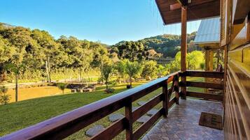 A covered outdoor area with a stone floor, wooden railing, and a view of a green landscape with trees and hills.
