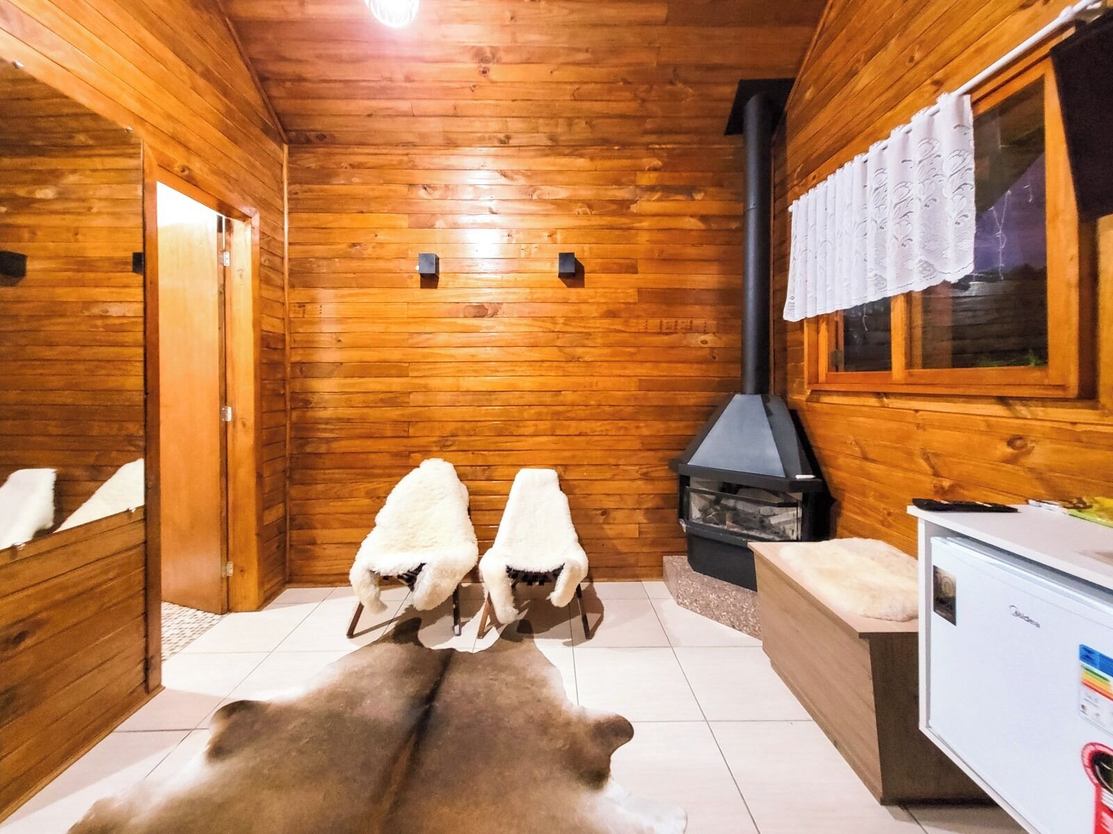 A wooden cabin interior with a fireplace, a sofa, and a refrigerator.