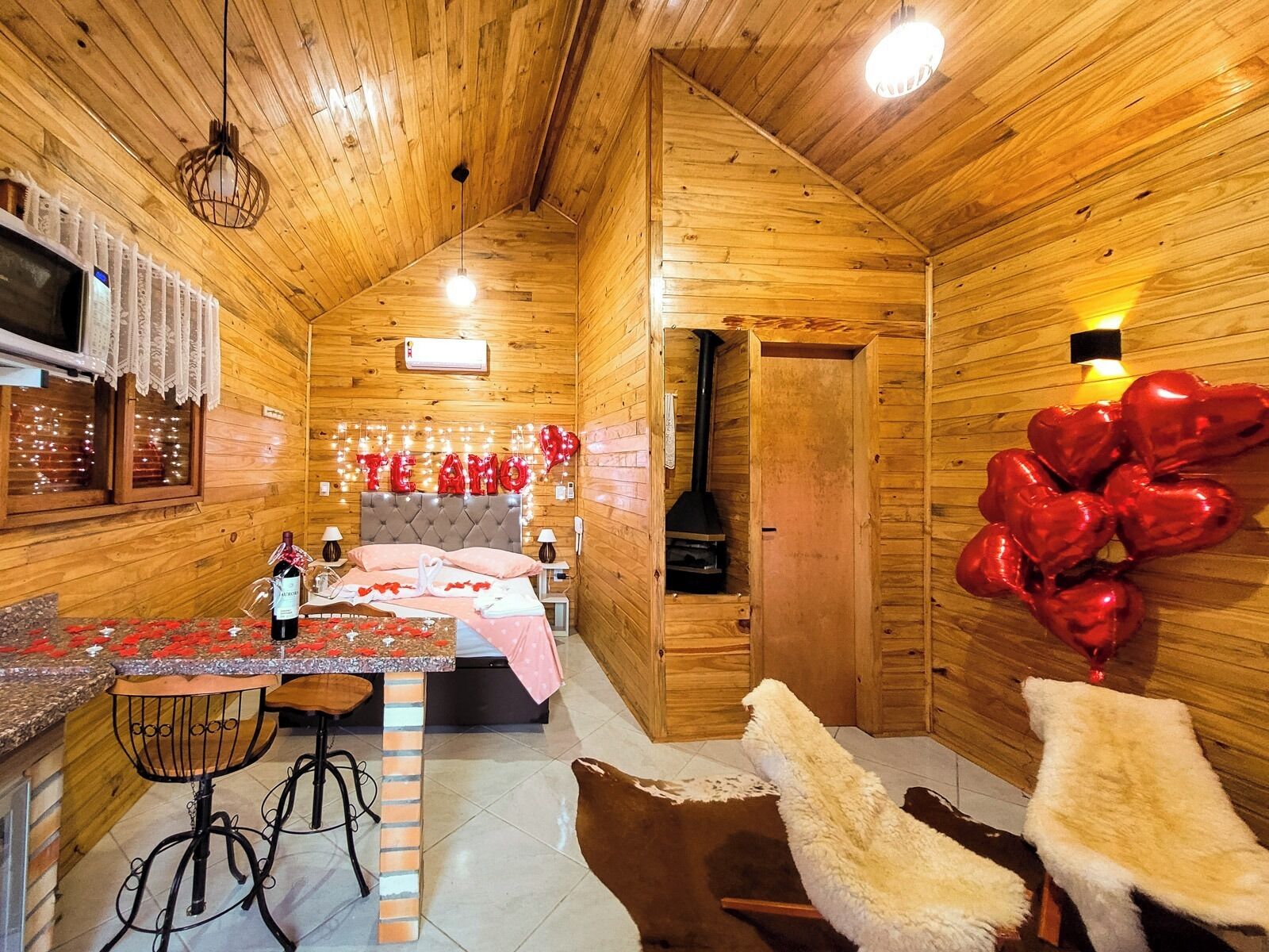 Una cabaña de madera acogedora con cama, una pequeña cocina y una chimenea.