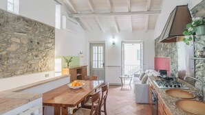 A kitchen with a stone wall, wooden table, chairs, a stove, and a sink.