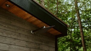 A wooden cabin with a metal door, surrounded by a forest. - Penner Cabin | Peaceful Wilderness Retreat (Minnow Drive, Dysart et al, ON)