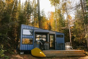 A modern cabin with large windows, a deck, and a yellow chair.