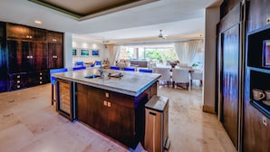 A spacious kitchen with a central island, a dining area with chairs, and a view of greenery outside. - Ground Floor Punta Mita Condo with Shared Pool (Punta Mita)