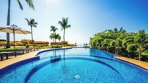 Une piscine d’un bleu éclatant, à bords incurvés, entourée de palmiers et surplombée d’un ciel dégagé.