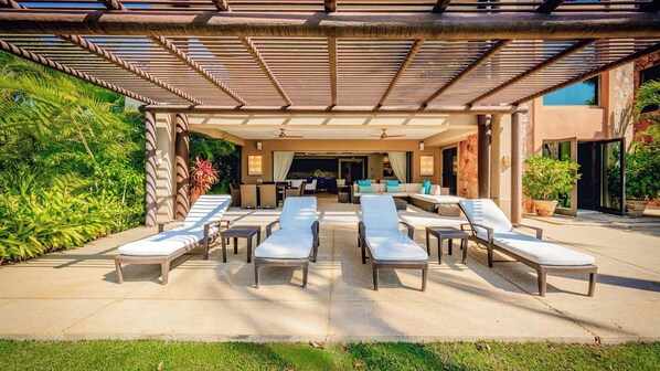 Un espace de détente extérieur avec des chaises longues, un coin salon abrité et une vue sur l’intérieur.