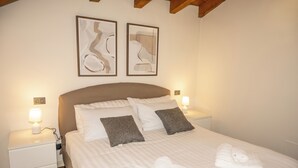 Una cama bien hecha con almohadas, una lámpara de noche y una toalla doblada sobre la mesita.