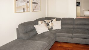 Un sofá seccional gris con cojines blancos y estampados, suelo de madera y arte abstracto en la pared.