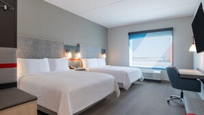 Ein Hotelzimmer mit zwei Betten, einem Schreibtisch, einem Sessel, einem Fernseher und einem großen Fenster.