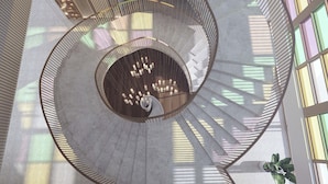 Eine Wendeltreppe mit einer offenen Mitte, umgeben von Wänden mit gemustertem Licht und großen Fenstern, die natürliches Licht hereinlassen.