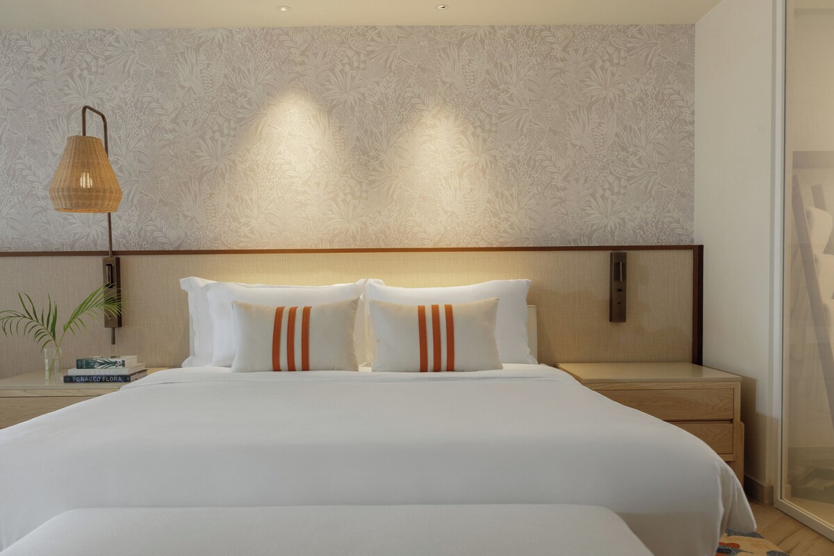 A hotel room with a large bed, a bedside table, a lamp, and a wall with a floral pattern.