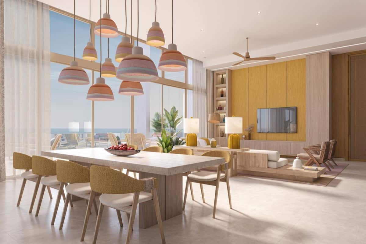 Un comedor moderno con una mesa grande, varias sillas, lámparas colgantes y vista al océano.