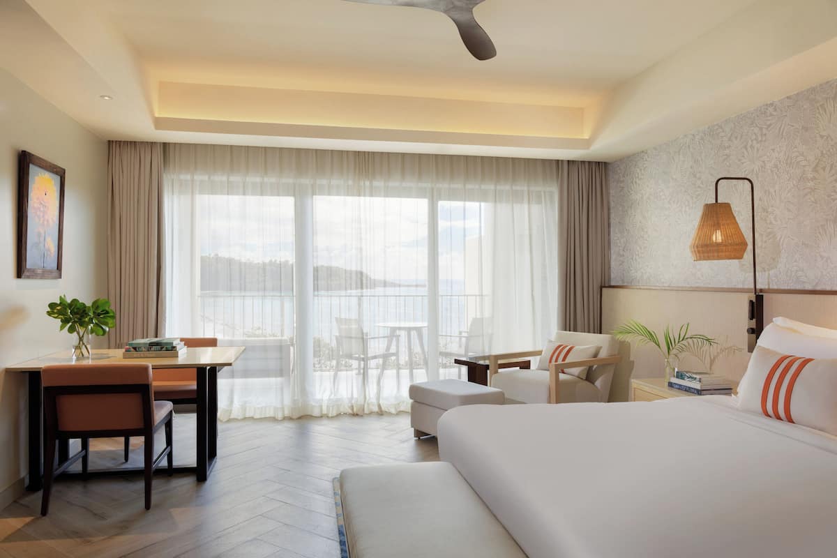 Habitación de hotel con cama, escritorio con sillas, mesa y vistas al exterior.