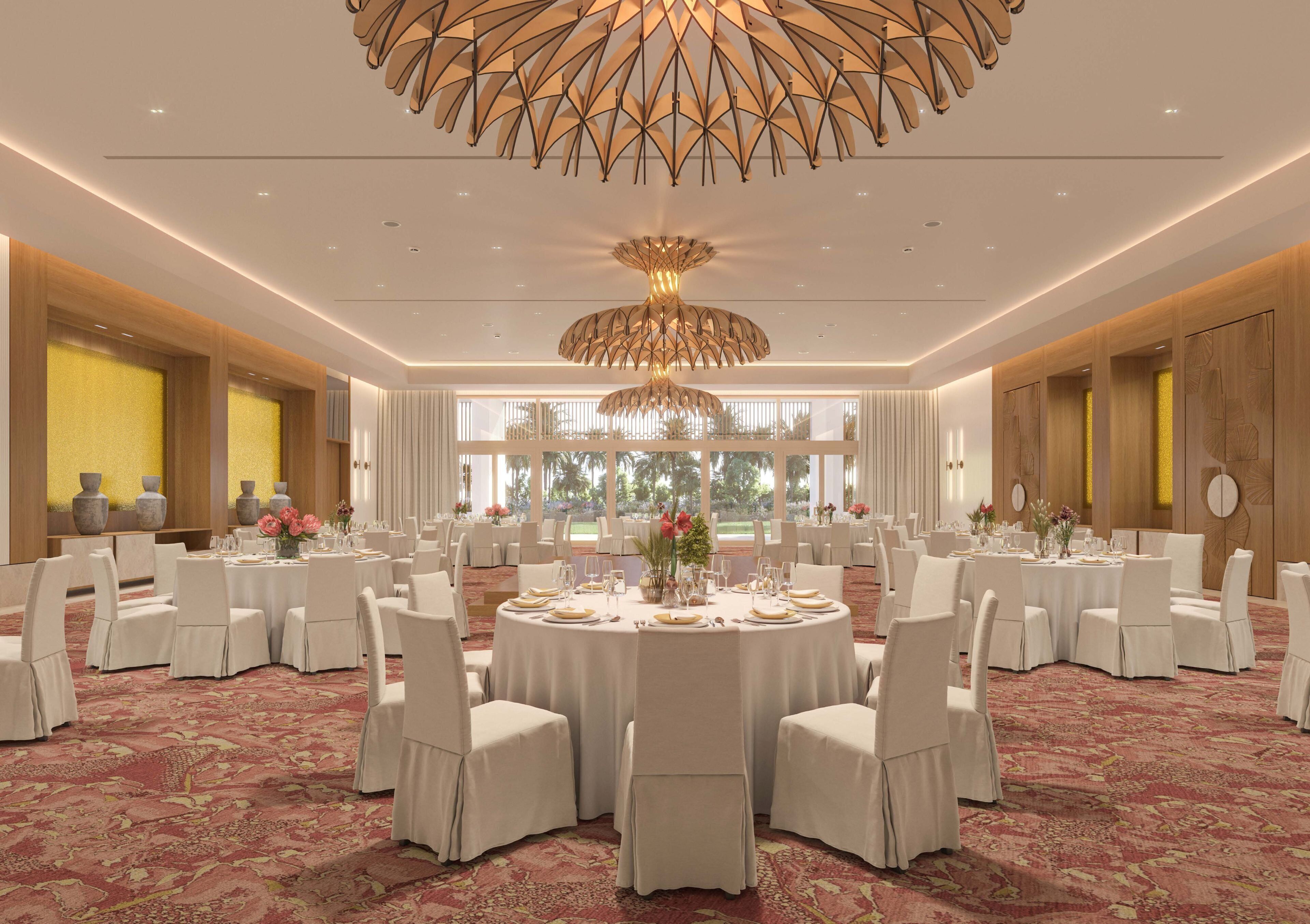 A banquet hall with round tables, white chairs, and a large chandelier.