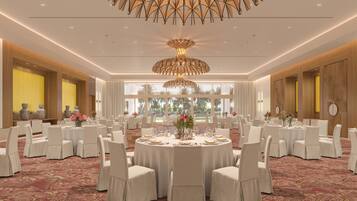 A banquet hall with round tables, white chairs, and a large chandelier.