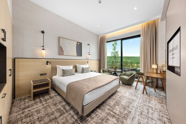 A hotel room with a large bed, a desk, a chair, a small table, and a view of the outdoors. - Crowne Plaza Istanbul Zeytinburnu By Ihg (Istanbul)
