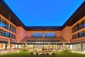 A modern building with a glass atrium, outdoor seating area, and a central garden feature. - Crowne Plaza Istanbul Zeytinburnu By Ihg (Istanbul)