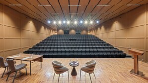 Konferenssitila, jossa on lava, rivi riveiltä tuoleja, puhujapönttö ja pöytä tuoleineen.