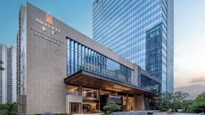 Ein modernes Hotelgebäude mit großen Glasfenstern, einem markanten Eingang und Hinweisschildern, die es als Finanzstadt-Hotel kennzeichnen.