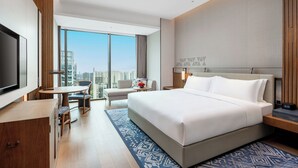 A modern hotel room with a large bed, a desk, a chair, a TV, and a view of the city. - Hualuxe Guiyang Financial City (Guiyang)