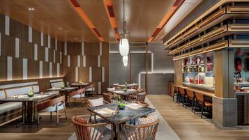Un interno ristorante moderno con pareti rivestite in legno, una sala da pranzo centrale con tavoli e sedie, e un'area bar con scaffali pieni di condimenti.