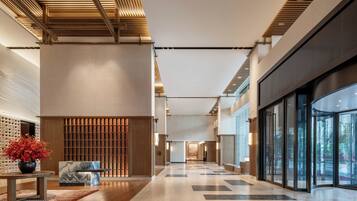 A modern hotel lobby with a high ceiling, a reception desk, a seating area, and large windows.