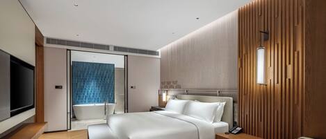 A modern hotel room with a large bed, a bedside table, a TV, and a bathroom with a shower and a blue-tiled wall.
