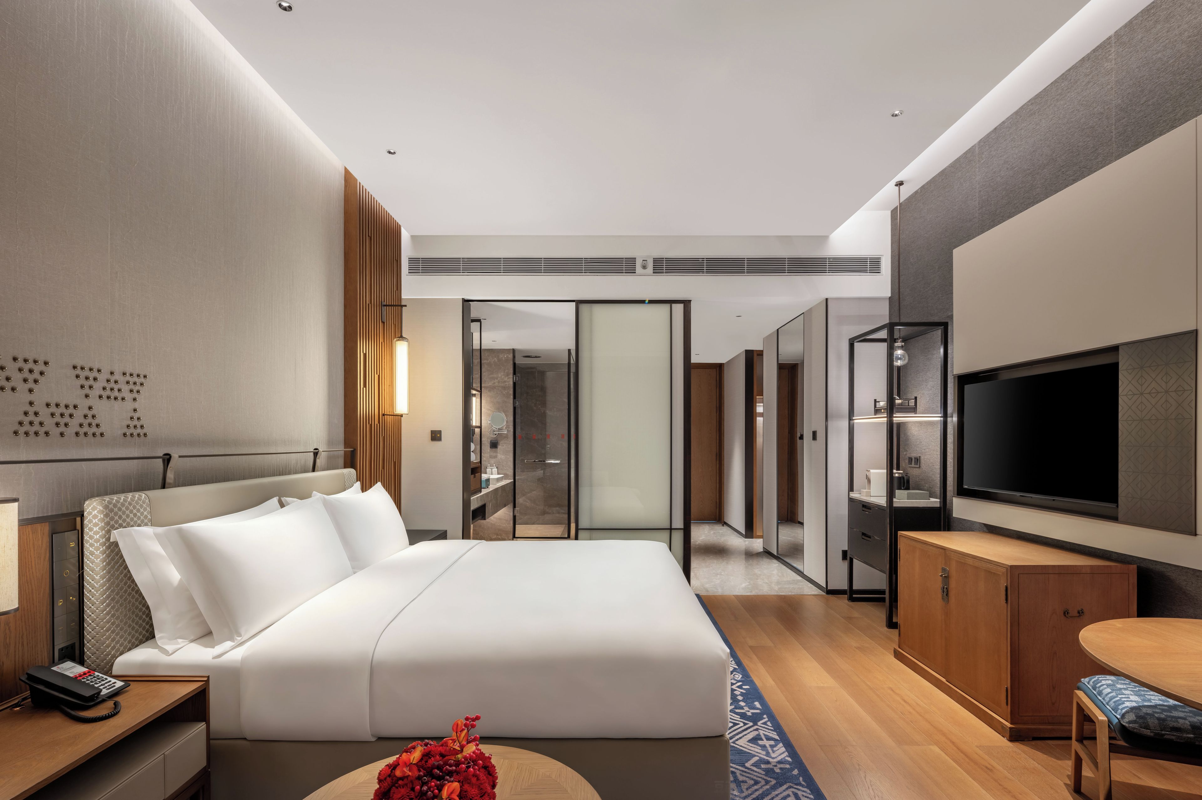 Ein modernes Hotelzimmer mit einem großen Bett, einem Schreibtisch mit Telefon, einem Fernseher und einer Sitzecke mit Tisch und Bank.