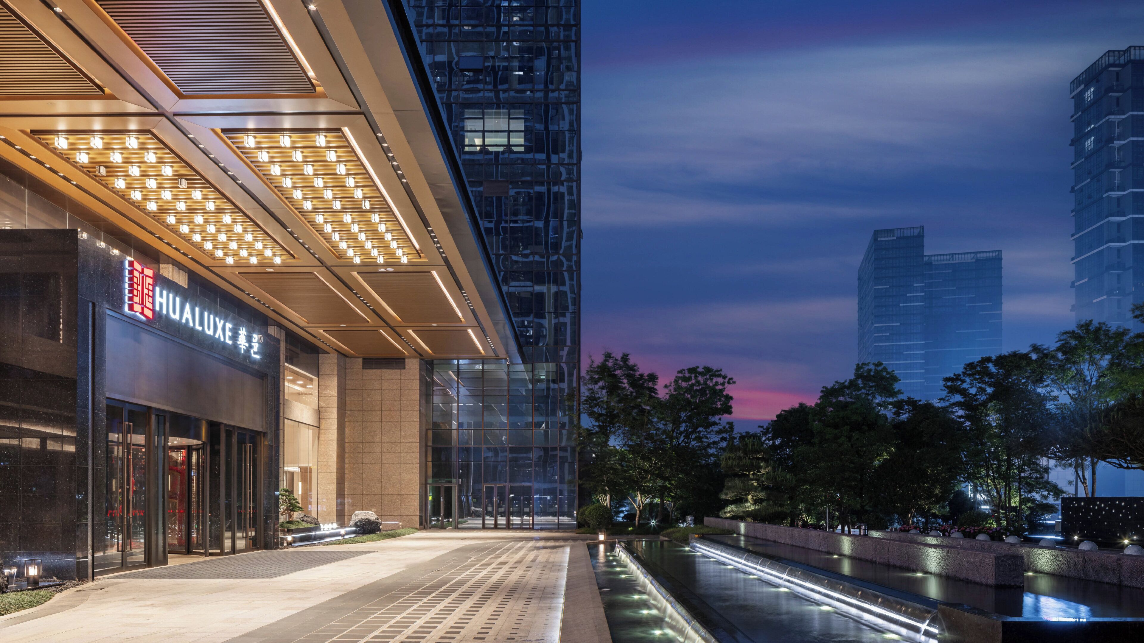 A modern building with a Hualux sign, a reflective glass facade, and a water feature in front.