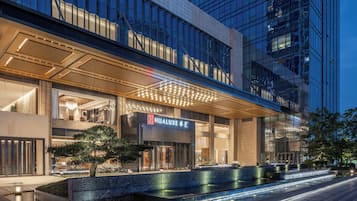 A modern hotel with a prominent entrance, a well-lit facade, and a water feature in front.