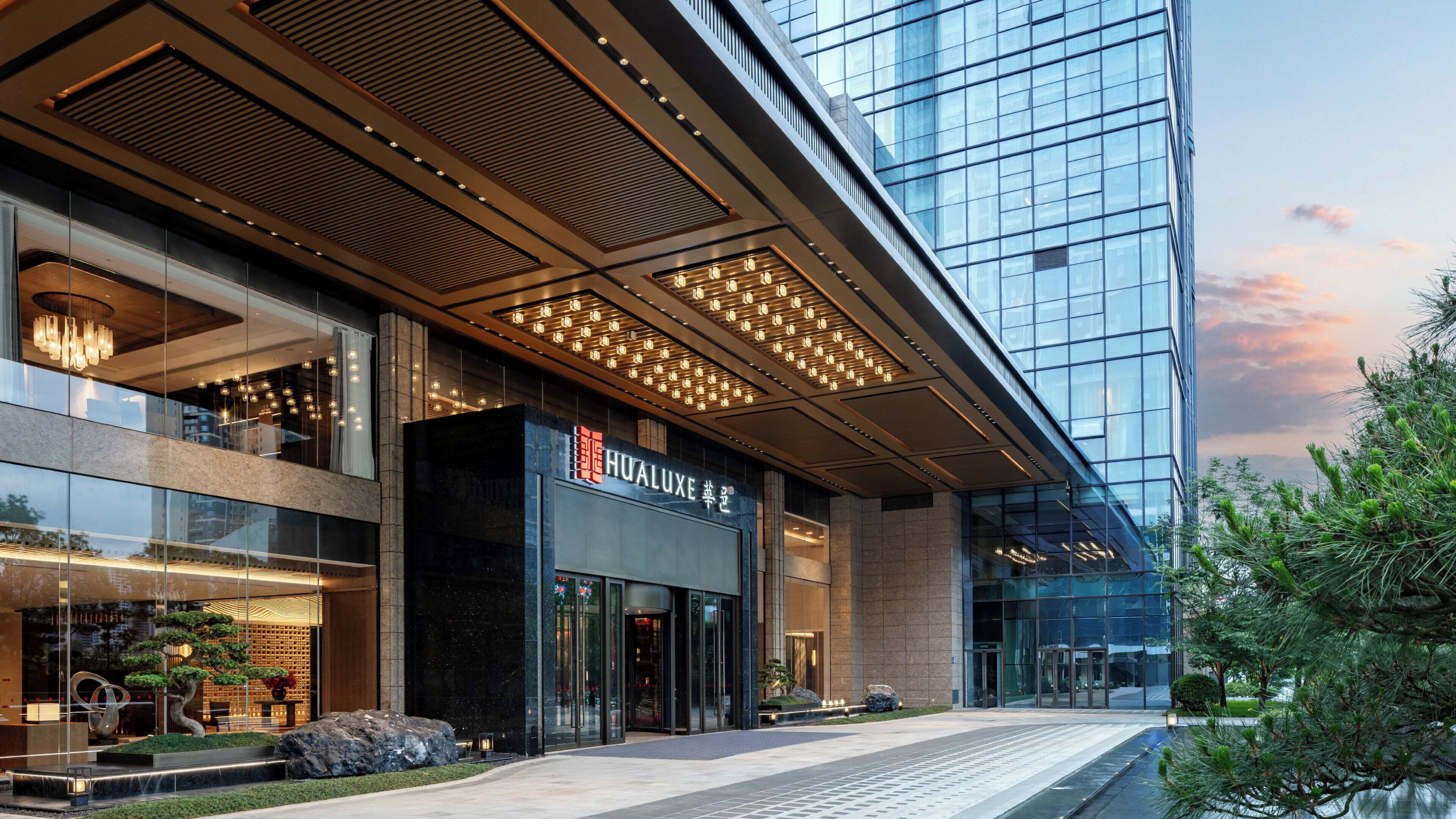 A modern hotel with a glass facade, a prominent entrance, and a well-lit lobby area.
