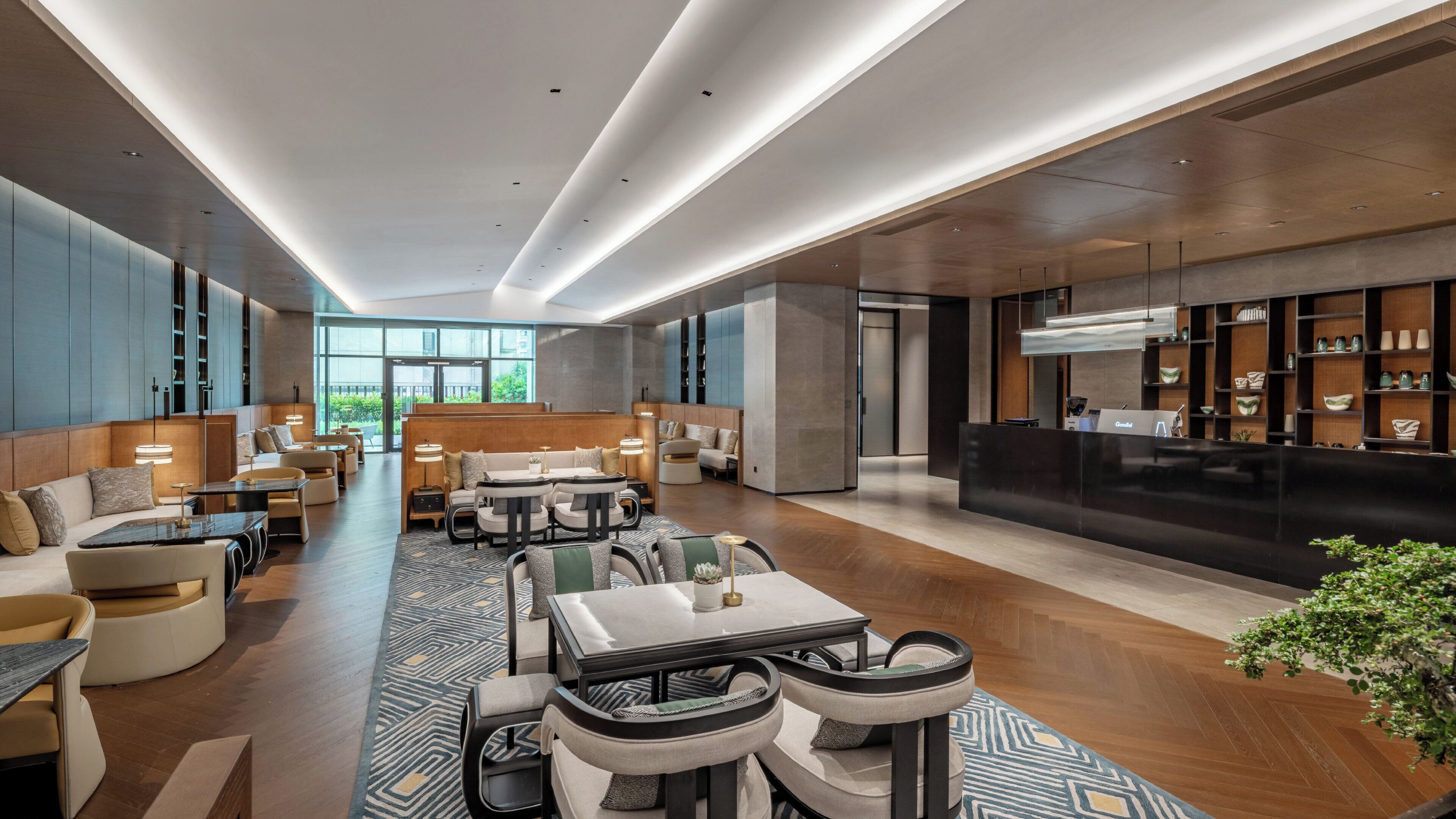 A modern hotel lobby with seating areas, a reception desk, and a view of the outdoors.